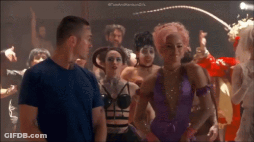 A Man In A Blue Shirt Is Standing In Front Of A Crowd Of People Dancing In A Club . GIF