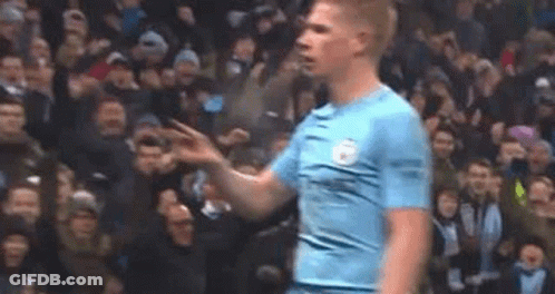 A Man In A Blue Shirt Is Standing In Front Of A Crowd Of People On A Soccer Field . GIF