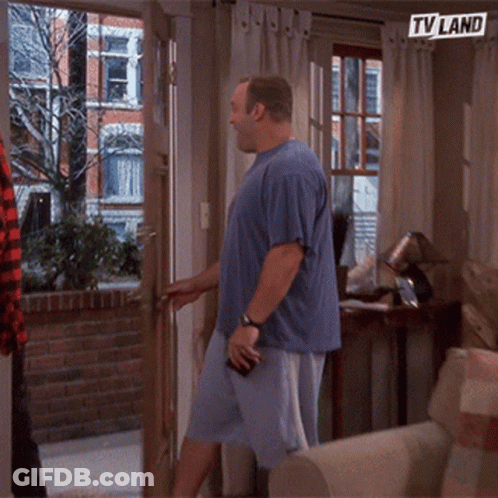A Man In A Blue Shirt Is Standing In Front Of A Door With A Tv Land Sign Above Him GIF