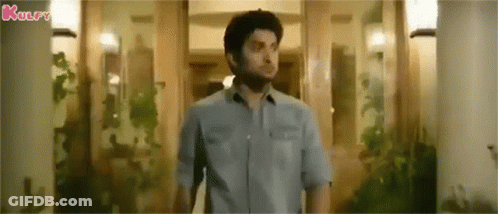A Man In A Blue Shirt Is Standing In Front Of A Doorway In A Room . GIF