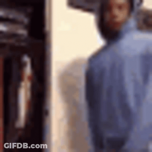 A Man In A Blue Shirt Is Standing In Front Of A Locker . GIF