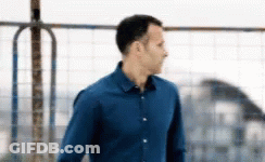A Man In A Blue Shirt Is Standing In Front Of A Metal Fence . GIF