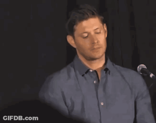 A Man In A Blue Shirt Is Standing In Front Of A Microphone With His Arm Raised GIF