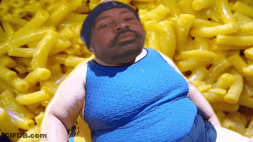A Man In A Blue Shirt Is Standing In Front Of A Pile Of Macaroni And Cheese GIF
