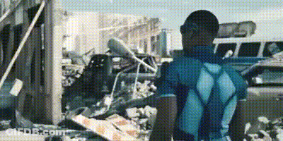 A Man In A Blue Shirt Is Standing In Front Of A Pile Of Rubble In A Parking Lot . GIF