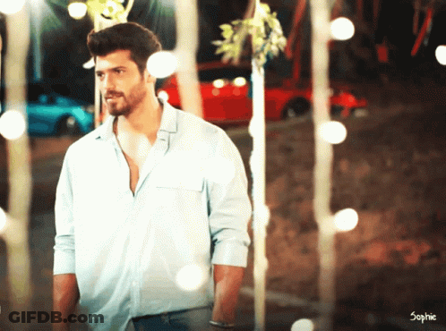 A Man In A Blue Shirt Is Standing In Front Of A Red Car And Trees GIF