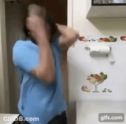 A Man In A Blue Shirt Is Standing In Front Of A Refrigerator With A Paper Towel Holder On It . GIF