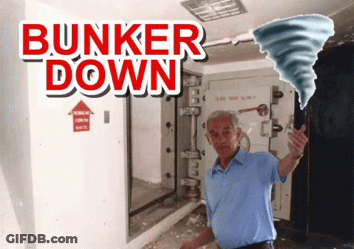 A Man In A Blue Shirt Is Standing In Front Of A Sign That Says " Bunker Down " GIF