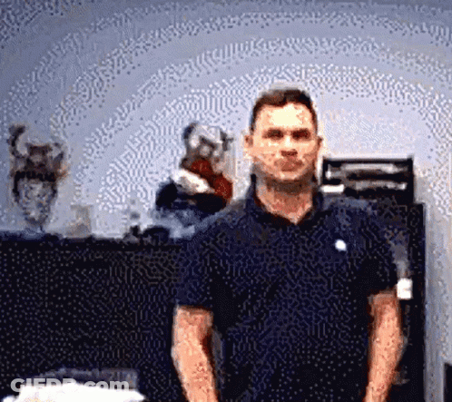 A Man In A Blue Shirt Is Standing In Front Of A Vase GIF
