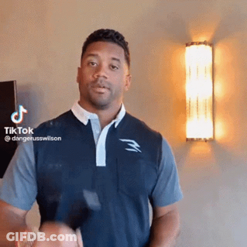 A Man In A Blue Shirt Is Standing In Front Of A Wall With A Tiktok Logo On It . GIF