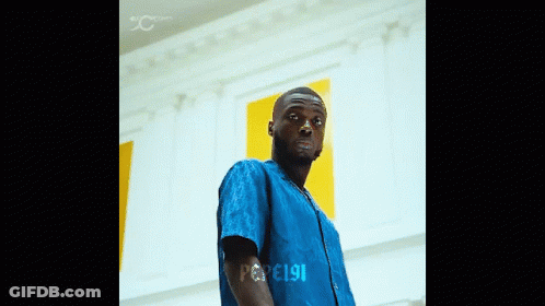 A Man In A Blue Shirt Is Standing In Front Of A Wall With The Number 191 On His Arm GIF