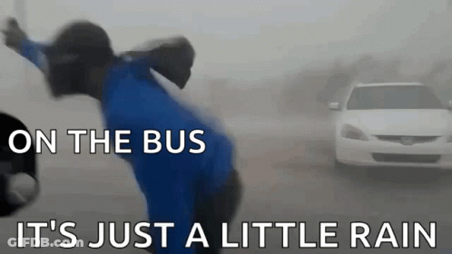 A Man In A Blue Shirt Is Standing In Front Of A White Car With The Words On The Bus It 'S Just A Little Rain GIF