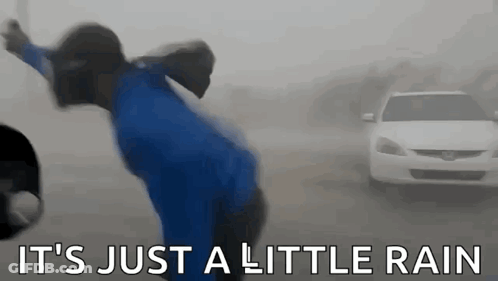 A Man In A Blue Shirt Is Standing In The Rain In Front Of A Car . GIF