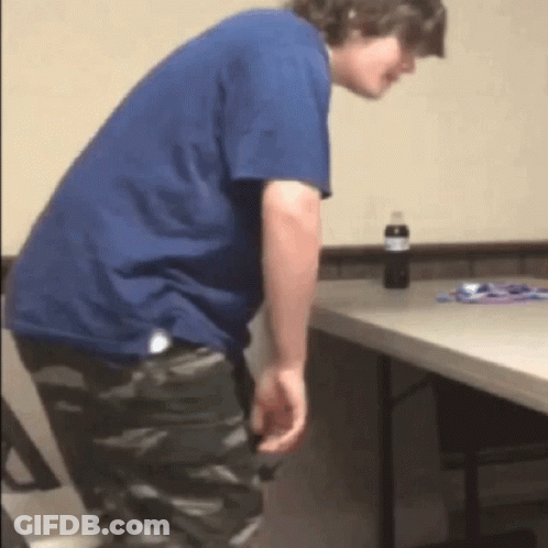 A Man In A Blue Shirt Is Standing Next To A Folding Table GIF