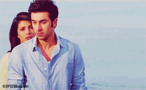 A Man In A Blue Shirt Is Standing Next To A Woman In A White Sweater GIF