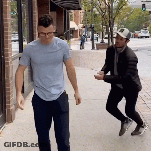 A Man In A Blue Shirt Is Standing Next To Another Man GIF