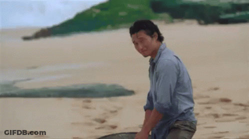 A Man In A Blue Shirt Is Standing On A Beach Holding A Fishing Net . GIF
