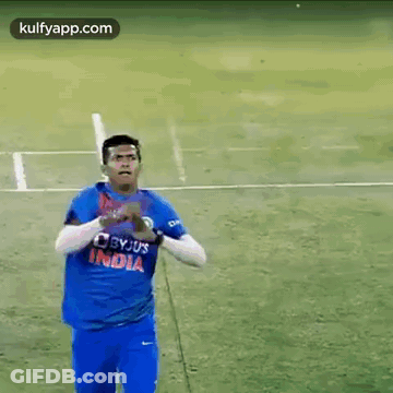 A Man In A Blue Shirt Is Standing On A Field Holding A Ball . GIF