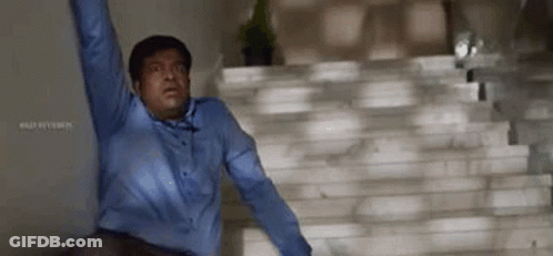 A Man In A Blue Shirt Is Standing On A Set Of Stairs With His Arms In The Air . GIF