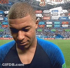 A Man In A Blue Shirt Is Standing On A Soccer Field With Ads For Qatar Coca Cola And Visa In The Background GIF