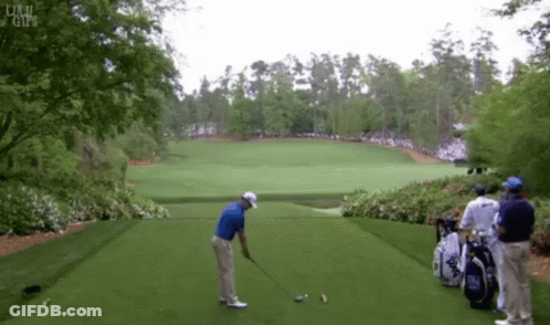 A Man In A Blue Shirt Is Swinging A Golf Club On A Green Field GIF
