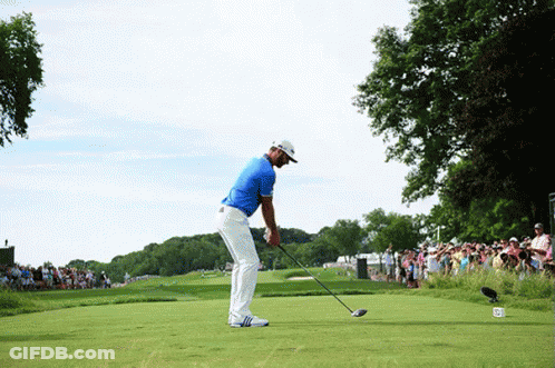 A Man In A Blue Shirt Is Swinging A Golf Club On A Green GIF