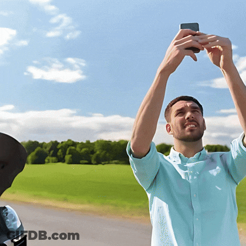 A Man In A Blue Shirt Is Taking A Picture Of A Field With His Phone GIF