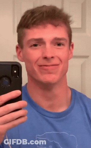 A Man In A Blue Shirt Is Taking A Selfie In Front Of A Mirror GIF