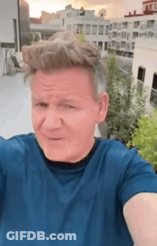 A Man In A Blue Shirt Is Taking A Selfie On A Rooftop With A City In The Background . GIF