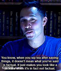 A Man In A Blue Shirt Is Talking In Front Of A Shelf Of Books GIF
