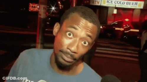 A Man In A Blue Shirt Is Talking Into A Microphone In Front Of A Sign That Says Ice Cold Beer GIF