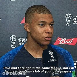 A Man In A Blue Shirt Is Talking Into A Microphone With A Bud Logo In The Background GIF