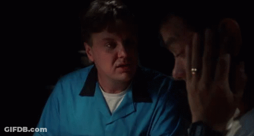 A Man In A Blue Shirt Is Talking To Another Man In A Dark Room . GIF