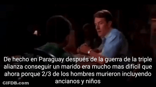 A Man In A Blue Shirt Is Talking To Another Man In A Dark Room In Spanish GIF