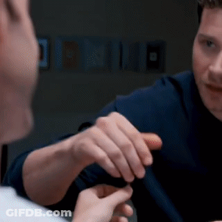 A Man In A Blue Shirt Is Talking To Another Man In A Dark Room GIF