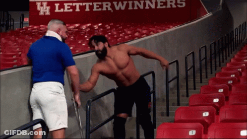 A Man In A Blue Shirt Is Talking To Another Man In Front Of A Sign That Says Letterwinners On It GIF