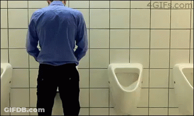 A Man In A Blue Shirt Is Urinating In A Bathroom GIF