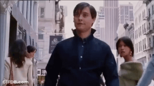 A Man In A Blue Shirt Is Walking Down A City Street With A Woman . GIF