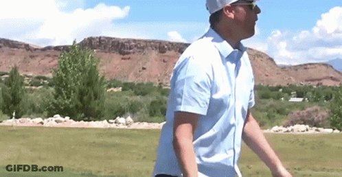 A Man In A Blue Shirt Is Walking On A Golf Course . GIF