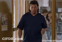 A Man In A Blue Shirt Is Walking Out Of A Doorway . GIF