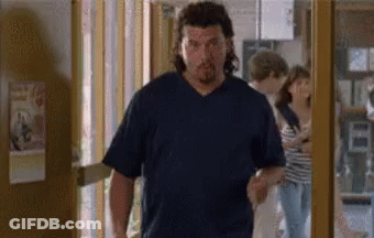 A Man In A Blue Shirt Is Walking Through A Doorway . GIF