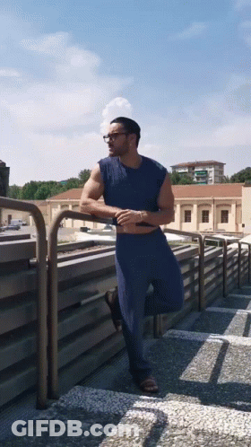 Man In Blue Shirt Leaning On Balcony Railing GIF