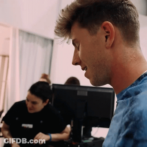 A Man In A Blue Shirt Looks At A Computer Screen GIF
