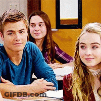 A Man In A Blue Shirt Sits At A Table Next To Two Women GIF