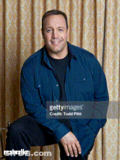 A Man In A Blue Shirt Sits In Front Of A Curtain GIF