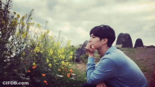 A Man In A Blue Shirt Sits In Front Of Flowers GIF