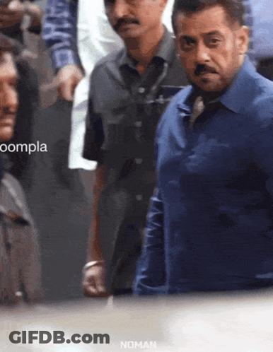 A Man In A Blue Shirt Stands In A Crowd With The Word Noman On The Bottom GIF