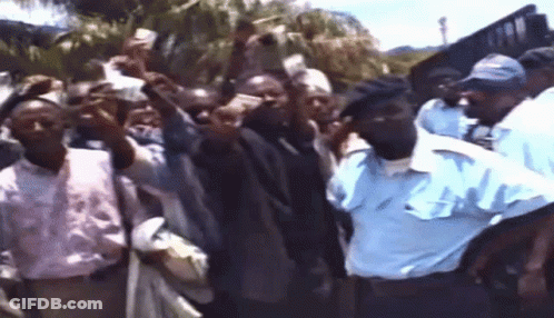 A Man In A Blue Shirt Stands In Front Of A Crowd GIF