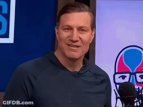 A Man In A Blue Shirt Stands In Front Of A Microphone In Front Of A Sign That Says S GIF