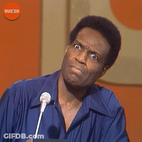 A Man In A Blue Shirt Stands In Front Of A Microphone With Buzzr Written On The Bottom GIF
